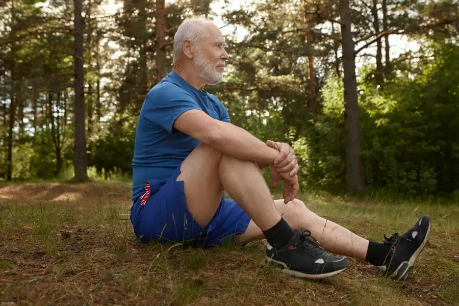 Älterer Mann mit Gonarthrose entspannt sich nach dem morgendlichen Training in der Natur